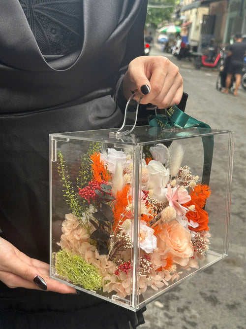 Side view of orange and peach dried roses arranged in an acrylic flower suitcase